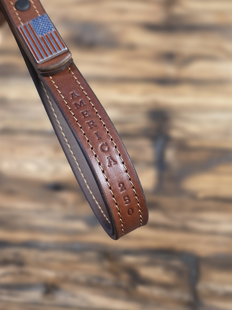 Brown leather strap with American flag and 'America 250' text on a blurred natural background