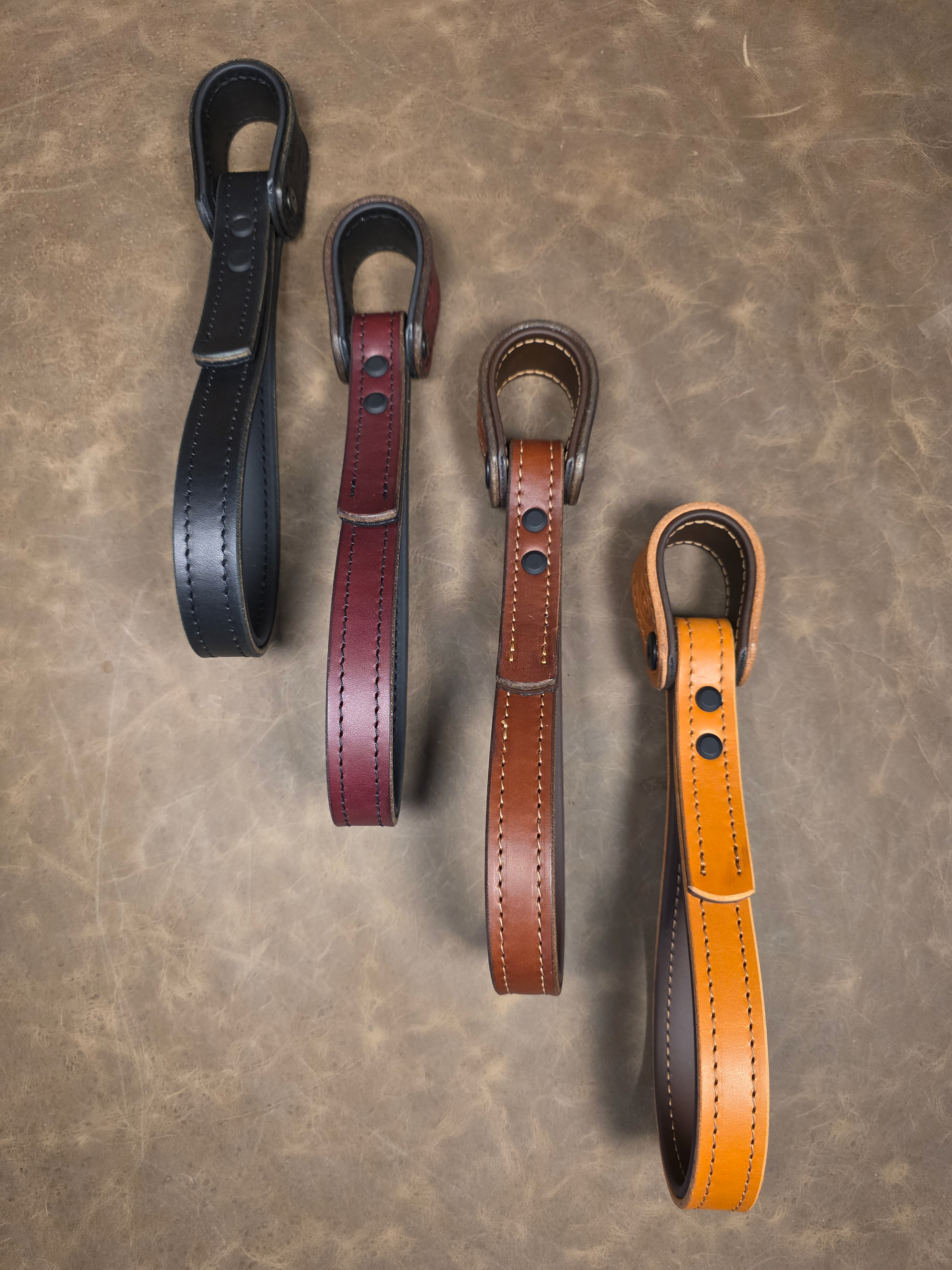 Four leather straps in black, oxblood, brown, and russet on a textured surface