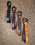 Four leather straps in black, oxblood, brown, and russet on a textured surface