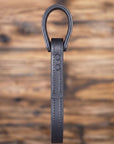 Black leather truck grab handle or vehicle entry assist strap with metal hardware against a blurred wooden background