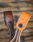 Closeups of two leather straps showcasing the Giddyupz logo and Hellhound logo with stitching details on a blurred background