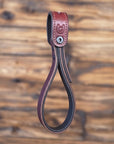 Oxblood leather vehicle entry assist strap with metal hardware against a blurred wooden background - front view
