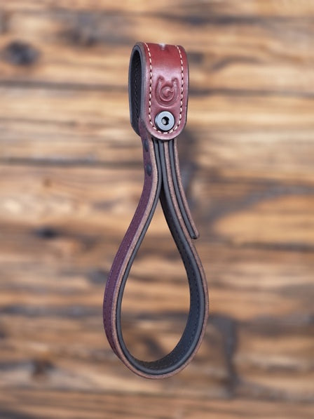 Oxblood leather strap with a metal bolt against a blurred wooden background