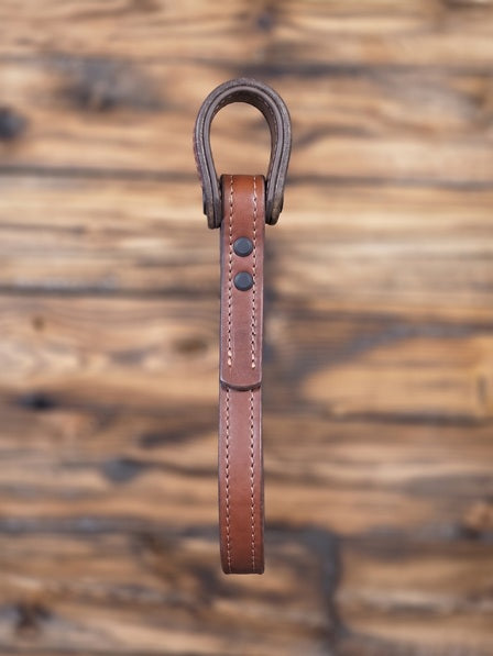 Brown leather vehicle entry assist strap with metal hardware against a blurred wooden background - side view