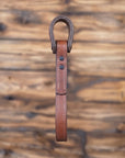 Brown leather vehicle entry assist strap with metal hardware against a blurred wooden background - side view