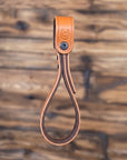 Tan leather vehicle entry assist strap with metal hardware against a blurred wooden background - front view