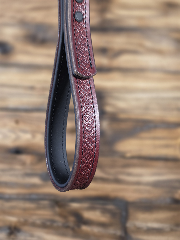 Oxblood leather grab strap with intricate pattern on a wooden surface