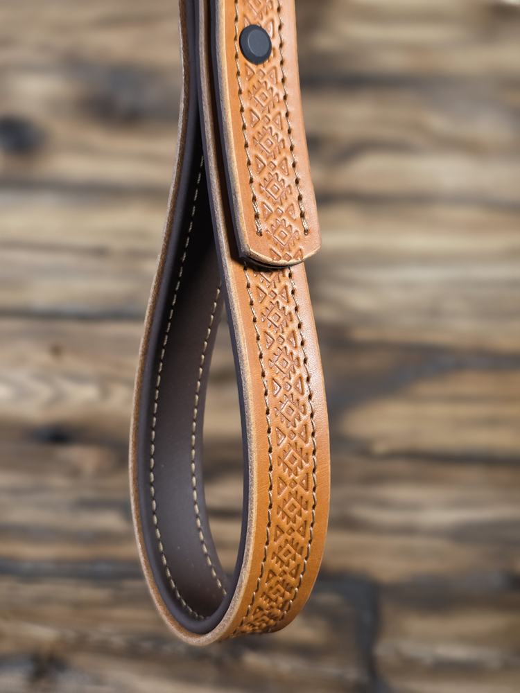 Close-up of a tan leather strap with intricate geometric pattern against a blurred wooden surface
