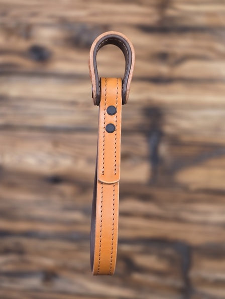 Tan leather vehicle entry assist strap with metal hardware against a blurred wooden background - side view