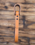 Tan leather vehicle entry assist strap with metal hardware against a blurred wooden background - side view