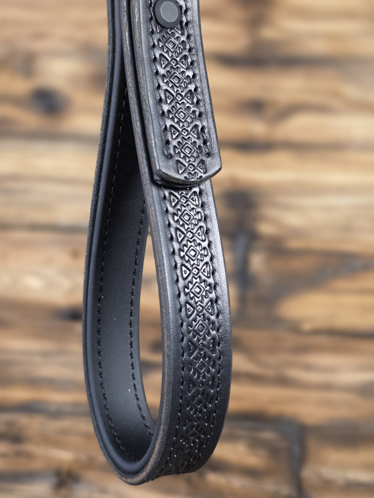 Black leather strap with intricate geometric pattern on a wooden background