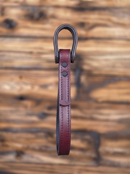 Oxblood leather vehicle entry assist strap with metal hardware against a blurred wooden background - side view