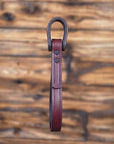Oxblood leather vehicle entry assist strap with metal hardware against a blurred wooden background - side view